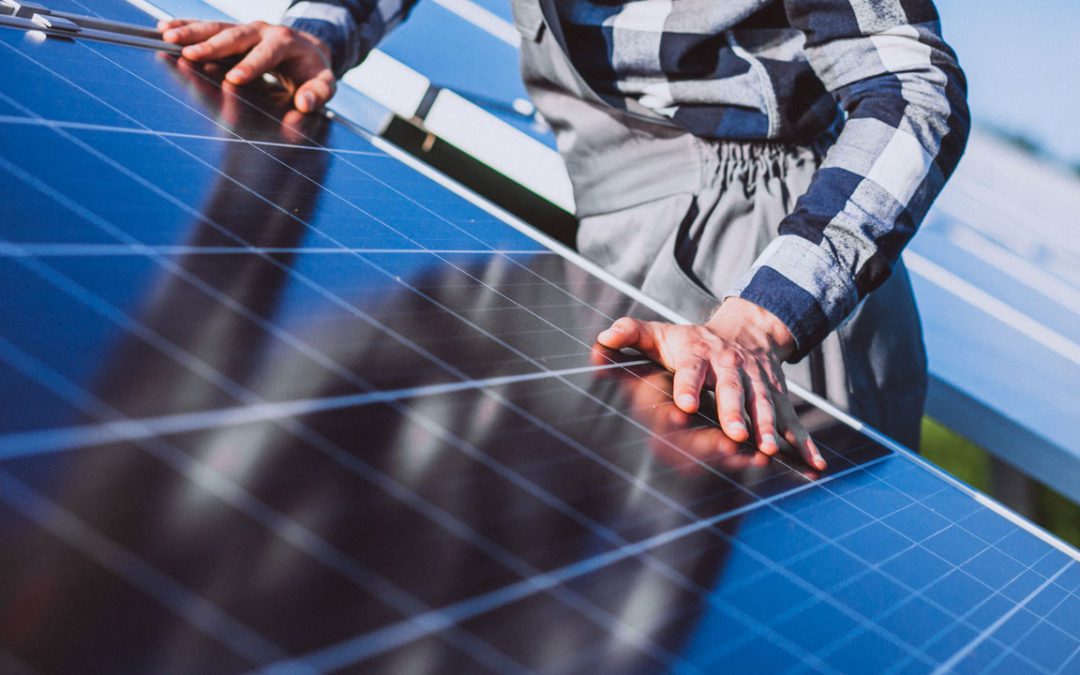 Manos de un hombre sobre una placa solar inclinada de una instalación fotovoltaica montada en suelo plano